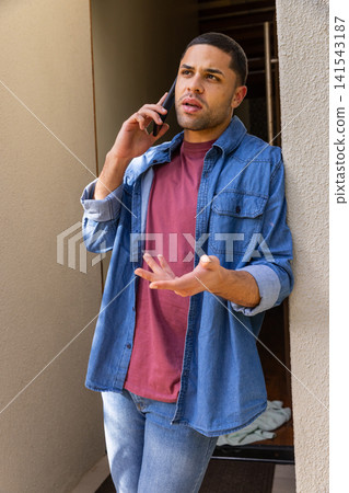 Man leaning against beige corridor wall, using smartphone, gesturing beside folded cloth Man leaning against beige corridor wall, using smartphone, gesturing beside folded cloth 141543187