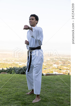 Punching forward african american male martial artist on grassy hilltop in white gi and belt Punching forward african american male martial artist on grassy hilltop in white gi and belt 141543209