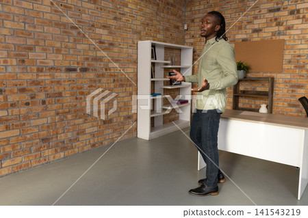 African american man standing in studio with shelving desk bulletin board, copy space African american man standing in studio with shelving desk bulletin board, copy space 141543219