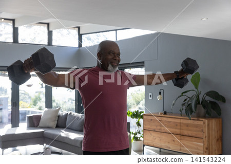 African american senior man in workout gear performing lateral raises at home holding dumbbells African american senior man in workout gear performing lateral raises at home holding dumbbells 141543224