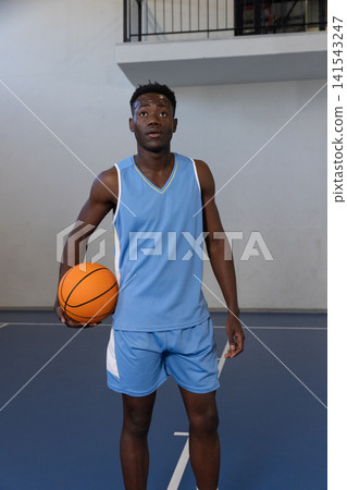African American male athlete in light blue basketball uniform on court holding orange basketball African American male athlete in light blue basketball uniform on court holding orange basketball 141543247