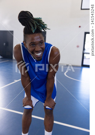 African american basketball player wearing blue-white uniform smiling on court African american basketball player wearing blue-white uniform smiling on court 141543248