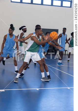 African american male player in green-white jersey passing orange basketball on court in gym African american male player in green-white jersey passing orange basketball on court in gym 141543250