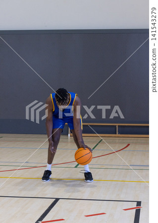 African american male dribbling orange basketball on wooden court in gym in blue and uniform African american male dribbling orange basketball on wooden court in gym in blue and uniform 141543279