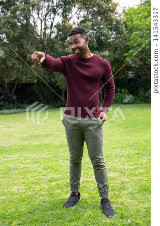 African american man standing on home lawn pointing beyond frame in maroon sweater African american man standing on home lawn pointing beyond frame in maroon sweater 141543317