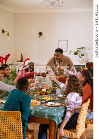 Diverse family and friends wearing santa hat raising glasses at table with roast chicken Diverse family and friends wearing santa hat raising glasses at table with roast chicken 141543318