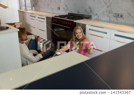 Couple sitting on floor in kitchen holding coffee mugs near red stove and marble backsplash Couple sitting on floor in kitchen holding coffee mugs near red stove and marble backsplash 141543367