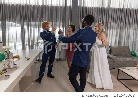 Newlyweds with friends raising champagne flutes near buffet table at lounge in formal attire Newlyweds with friends raising champagne flutes near buffet table at lounge in formal attire 141543368