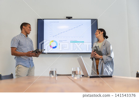 Diverse colleagues presenting charts on tablets and wall-mounted display in office 141543376