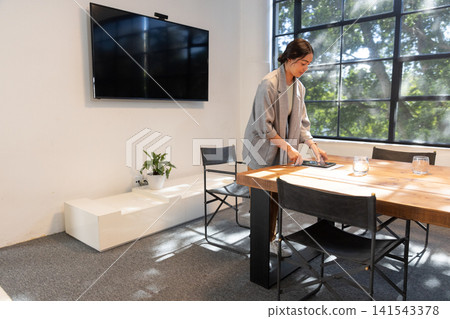 Woman standing by wooden table in meeting room arranging tablet near glasses, copy space Woman standing by wooden table in meeting room arranging tablet near glasses, copy space 141543378
