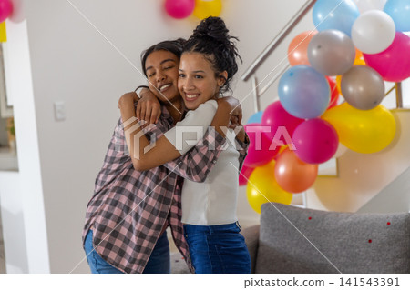 Diverse mom and teenage daughter hugging near staircase railing in living room Diverse mom and teenage daughter hugging near staircase railing in living room 141543391