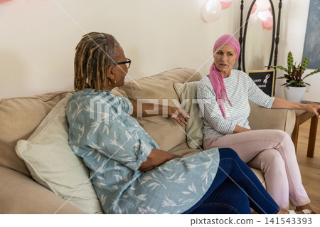 Diverse female friends talking at home on sofa with balloons and chalkboard sign Diverse female friends talking at home on sofa with balloons and chalkboard sign 141543393