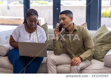 Diverse coworkers collaborating on laptop and smartphone in office wearing business attire 141543397