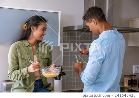 Diverse couple cooking together in home kitchen, adding oil and whisking egg mixture in bowl 141543423