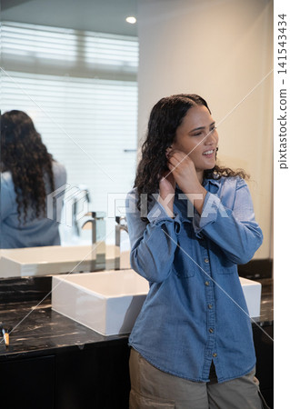 Woman adjusting earring at bathroom sink and countertop with makeup brush, faucet, copy space Woman adjusting earring at bathroom sink and countertop with makeup brush, faucet, copy space 141543434
