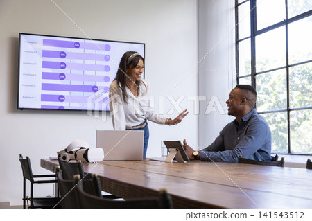 Diverse coworkers presenting data at meeting room with laptop, vr headset and bar charts Diverse coworkers presenting data at meeting room with laptop, vr headset and bar charts 141543512