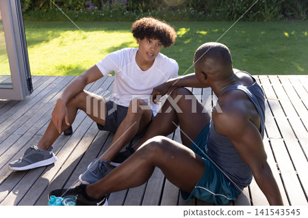 Diverse male friends wearing sportswear on wood deck at house with water bottles and mat Diverse male friends wearing sportswear on wood deck at house with water bottles and mat 141543545