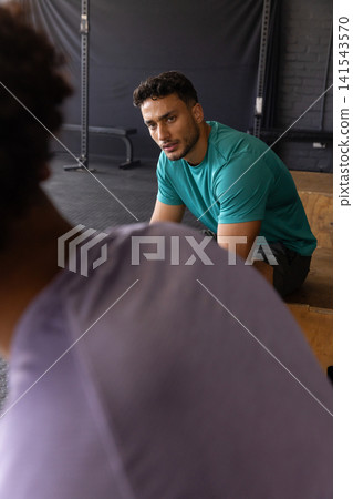 Hispanic male friends resting between exercises on plyometric box at gym with squat rack Hispanic male friends resting between exercises on plyometric box at gym with squat rack 141543570