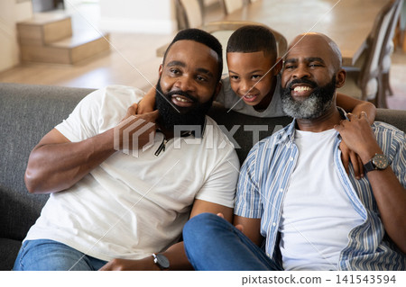 African American family sitting on dark gray sofa in bright living room near stacked chairs African American family sitting on dark gray sofa in bright living room near stacked chairs 141543594