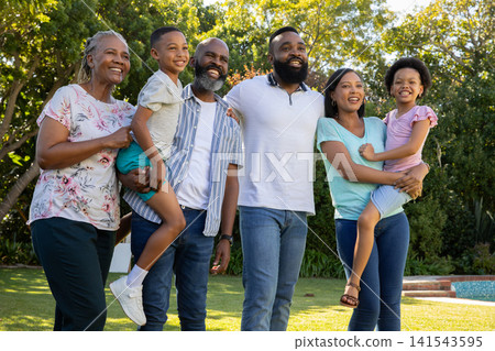 Diverse extended family standing together on well-kept grassy yard in backyard by swimming pool Diverse extended family standing together on well-kept grassy yard in backyard by swimming pool 141543595