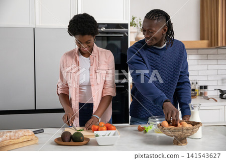African american couple cooking at kitchen island chopping green onions and selecting eggs African american couple cooking at kitchen island chopping green onions and selecting eggs 141543627