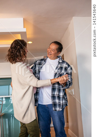 Diverse couple dancing near kitchen island with bar stools at home under recessed lights Diverse couple dancing near kitchen island with bar stools at home under recessed lights 141543640