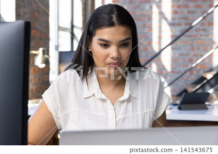 Woman typing on laptop at wooden desk in office loft with monitor and brick wall 141543675