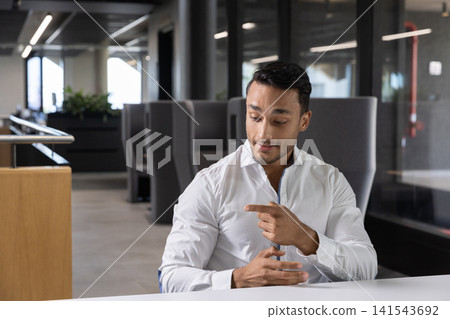 Man sitting at white table in modern office lounge gesturing next to glass partitions Man sitting at white table in modern office lounge gesturing next to glass partitions 141543692