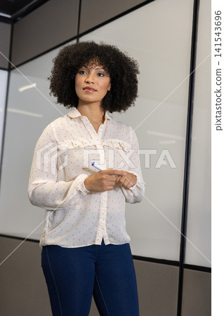 Mid adult african american woman standing in meeting room with marker at glass whiteboard Mid adult african american woman standing in meeting room with marker at glass whiteboard 141543696
