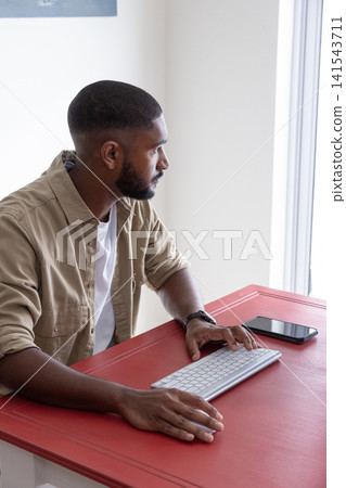 African american man using keyboard and smartphone at desk by window wearing watch, copy space African american man using keyboard and smartphone at desk by window wearing watch, copy space 141543711