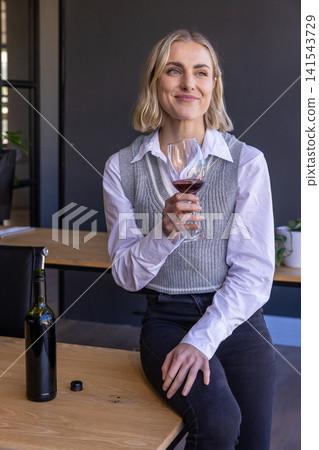 Female drinking red wine beside wine bottle on table in modern tasting room 141543729