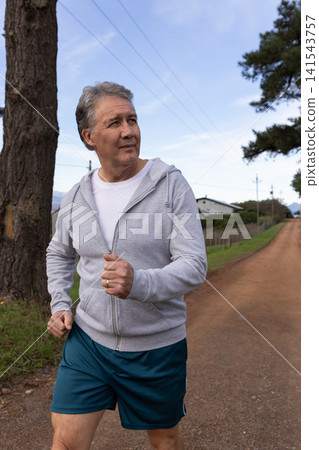 Man jogging along rural dirt road wearing zip-up hoodie and teal running shorts Man jogging along rural dirt road wearing zip-up hoodie and teal running shorts 141543757