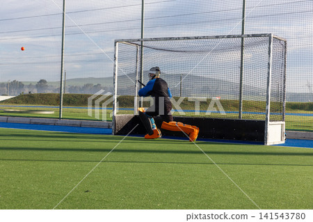 Mid adult man crouching low before goal on turf, blocking ball with stick, copy space 141543780