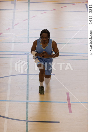 African american male athlete performing deep lunge on basketball court wearing light blue uniforms 141543811