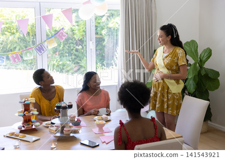 Diverse female friends celebrating baby shower at dining table with cupcakes, banners, copy space Diverse female friends celebrating baby shower at dining table with cupcakes, banners, copy space 141543921