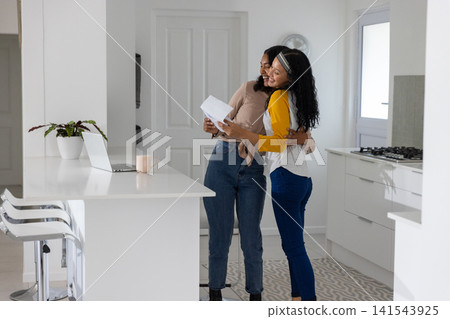 Mother hugging teenage daughter and reviewing papers in white kitchen with laptop Mother hugging teenage daughter and reviewing papers in white kitchen with laptop 141543925