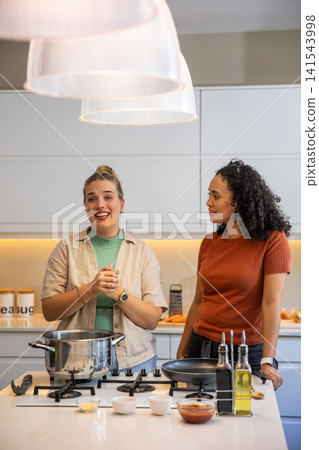 Diverse female friends cooking together at modern kitchen island using spices, pan and olive oil Diverse female friends cooking together at modern kitchen island using spices, pan and olive oil 141543998