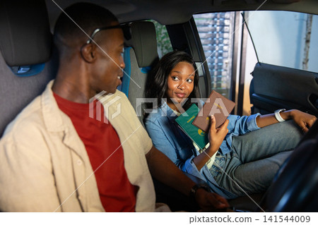 African American couple holding passports and talking inside parked car near metal shutter African American couple holding passports and talking inside parked car near metal shutter 141544009