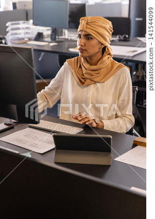 Mid adult indian woman working on tablet at open-plan office desk with monitor 141544099