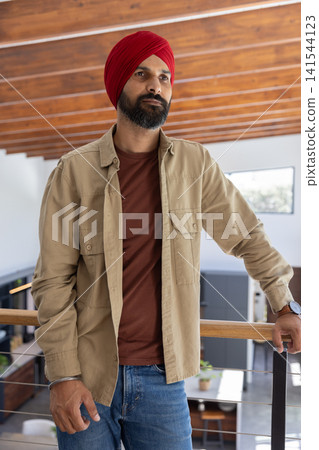 Indian man standing on balcony railing inside modern home overlooking living area, potted plant Indian man standing on balcony railing inside modern home overlooking living area, potted plant 141544123