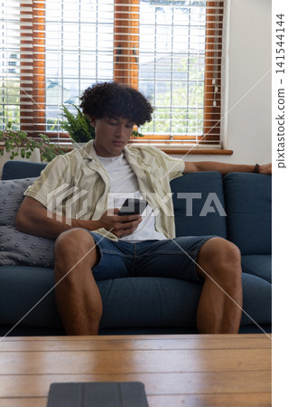 Male checking smartphone while sitting on sofa in living room with tablet on coffee table Male checking smartphone while sitting on sofa in living room with tablet on coffee table 141544144