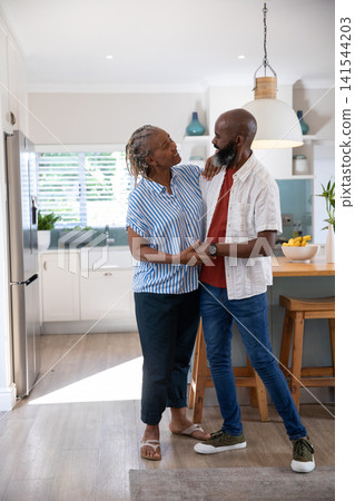 Senior African American couple standing in modern kitchen with banana bowl on island, holding hands Senior African American couple standing in modern kitchen with banana bowl on island, holding hands 141544203