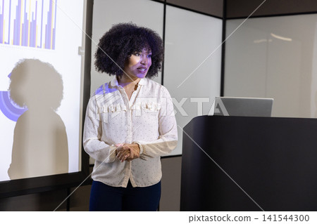 Mid adult woman in blouse presenting bar and pie charts on screen at conference podium Mid adult woman in blouse presenting bar and pie charts on screen at conference podium 141544300