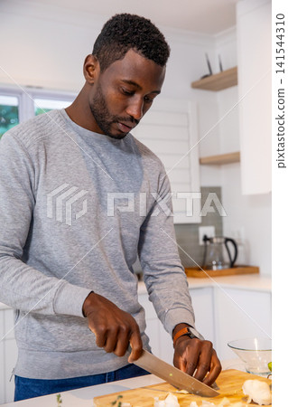 African american man slicing cauliflower florets holding chef's knife on cutting board in kitchen African american man slicing cauliflower florets holding chef's knife on cutting board in kitchen 141544310