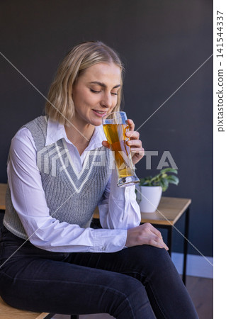 Woman in her 30s sitting in lounge on chair holding beer glass Woman in her 30s sitting in lounge on chair holding beer glass 141544337