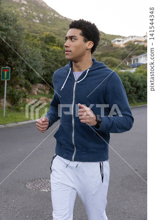 African american man running along paved road on hillside, checking smartwatch African american man running along paved road on hillside, checking smartwatch 141544348