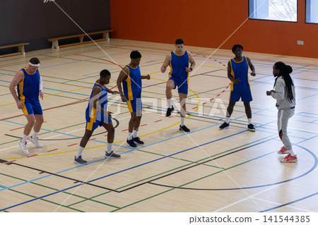 Diverse male basketball team wearing blue jerseys warming up on court with coach in tracksuit Diverse male basketball team wearing blue jerseys warming up on court with coach in tracksuit 141544385