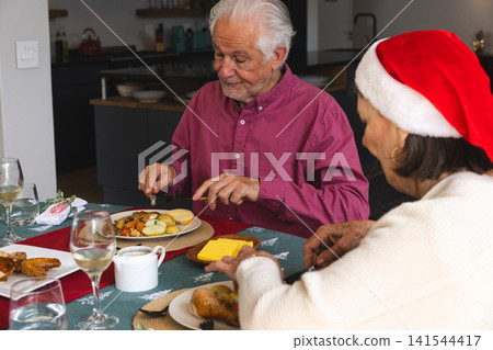 Senior couple cutting potatoes and adding cheese to bread at home holiday table with roast chicken Senior couple cutting potatoes and adding cheese to bread at home holiday table with roast chicken 141544417