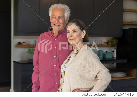 Senior couple standing together in contemporary kitchen, smiling near dark cabinets and teal kettle Senior couple standing together in contemporary kitchen, smiling near dark cabinets and teal kettle 141544419