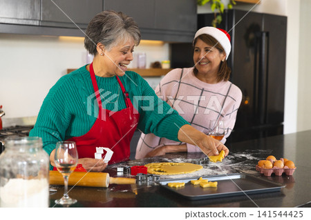 Senior mother and adult daughter cutting holiday cookie dough on counter with rolling pin, cutters Senior mother and adult daughter cutting holiday cookie dough on counter with rolling pin, cutters 141544425